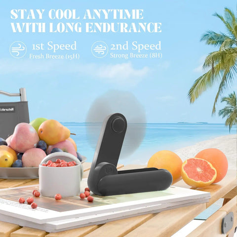 Black 2 In 1 Portable Handheld Fan USB Rechargeable Personal Mini Fan With 8 To 15 Hours Run Time Battery Operated on a table by the beach