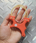 Ultra Compact Mini Slingshot With Flat And Round Bands In Red Nylon Fiber, Ambidextrous And Pocket Sized, held in hand for size reference.