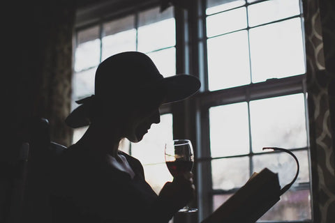 Silhouette of a person reading with a Rechargeable Clip On Book Light With Warm Eye Care LEDs by a window, holding a glass.