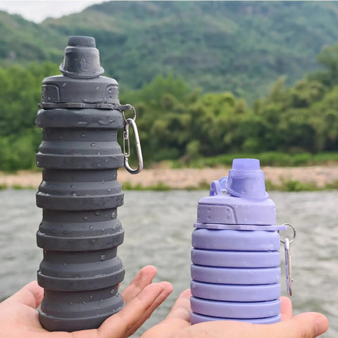 Two Pack Collapsible Silicone Water Bottles 500ml Each, Purple and Grey, held with mountaineering buckles, outdoor background