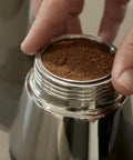 Hella Durable Stainless Steel Stovetop Espresso Maker For Rich Coffee Brews with coffee grounds being loaded into the filter.
