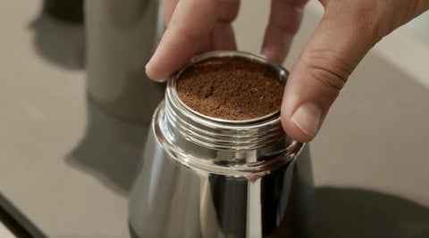 Hella Durable Stainless Steel Stovetop Espresso Maker For Rich Coffee Brews with coffee grounds being loaded into the filter.