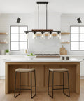 Modern Farmhouse 5 Light Linear Chandelier for Kitchen Island and Dining Room with Adjustable Rustic Pendant Light Black Metal Frame Real Wood Accent Clear Glass Shades Industrial Style Vibe hanging over kitchen island.