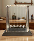 Cradle Balance Pendulum Balls Set With Black Base on wooden desk in home office. Kinetic fidget desk toy for stress relief.