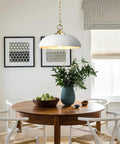 Top Shelf Matte White Farmhouse Pendant Light With Burnished Brass Accents illuminating a dining table with greens and decor.