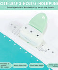 Three-Hole Mini Paper Puncher Portable Desktop Handheld Puncher placed with turquoise paper, showcasing ABS design and hole spacing.