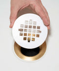 Rock Solid Universal Shower Drain Strainer In Durable White Plastic Snap Tite Cover Fits Standard Two Or Three Inch Drains being installed over a gold drain.