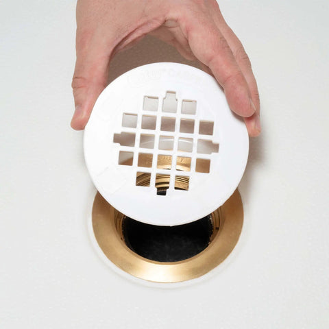 Rock Solid Universal Shower Drain Strainer In Durable White Plastic Snap Tite Cover Fits Standard Two Or Three Inch Drains being installed over a gold drain.