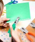 Child using Eight Piece Hole Punch Set With Shaped Punchers For Craft Lovers Handheld Metal Paper Punch With Grippy Handle on green paper.