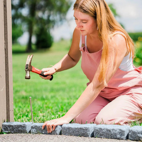 Person installing Greystone Faux Stone Landscape Edging Kit For Lawn And Garden Borders 40 Pack System with a hammer and spike