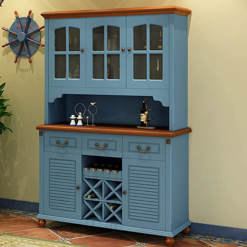 Blue cabinet with glass doors and wine storage, wooden top, displayed in a cozy room with nautical decor and plant.