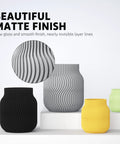 Front view of matte-finish ribbed vases in black, gray, yellow, and lime green on a white platform