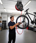 Hardcore Workhorse Retractable Air Hose Reel Runs 50 Ft Of Hybrid Polymer Tubing With Slick Auto Rewind Tech And Heavy Duty Steel Arm Wall Mounted Tight For Quick Shop Jobs That Never Snag, being used to inflate a bicycle tire.