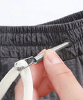 Close-up of No Fuss Drawstring Threader Tool Flexible Spring Loaded Bodkin threading a white cord into gray pants.