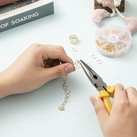 Hands using pliers with Over 1000 Open Jump Rings Kit With 40Pcs 12Mm Lobster Clasps And Jump Ring Opener for jewelry making on table.