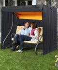 All Weather Yard Saver Swing Cover For Three Seaters And Garden Hammocks in black, protecting swing with seated couple outdoors