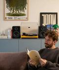 Bluetooth Bookshelf Speakers for Turntable With 60W RMS Power next to a turntable in a cozy room with a person reading