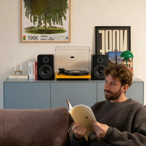 Bluetooth Bookshelf Speakers for Turntable With 60W RMS Power next to a turntable in a cozy room with a person reading