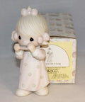 Ceramic figurine of a girl in a pink dress playing a harmonica, with a decorative box in the background.