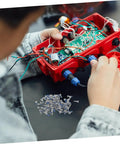 Person working on electronics with scattered screws from a Glasses Repair Screws Kit, 100 Piece Eyeglass Screw Set For Glasses And Sunglasses.