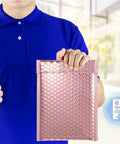 Person holding a rose gold metallic bubble mailer with self seal adhesive, part of a 50 pack padded poly mailers for Valentine shipping.