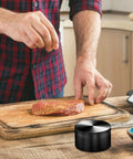 Man seasoning meat with 3 Inch Manual Spice Grinder For Kitchen With 3 Piece Design No Mesh Screen Durable Zinc Alloy Construction Sharp Teeth For Consistent Grinding Grinds Like A Boss Compact Easy To Clean Black on cutting board.