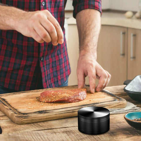 Man seasoning meat with 3 Inch Manual Spice Grinder For Kitchen With 3 Piece Design No Mesh Screen Durable Zinc Alloy Construction Sharp Teeth For Consistent Grinding Grinds Like A Boss Compact Easy To Clean Black on cutting board.