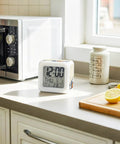 Real Deal Cube Digital Alarm Clock Straight Up Showcasing A Fresh Seven Color Led Night Light on a kitchen counter next to a microwave.