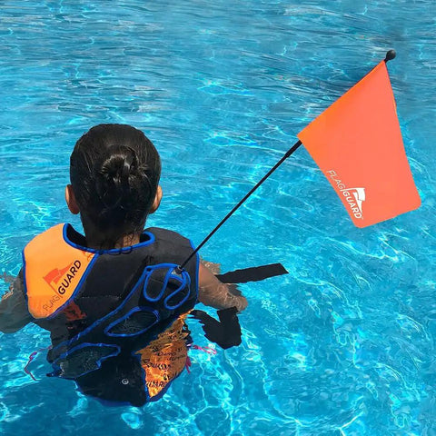 Child wearing bright orange life jacket safety flag with adjustable pouch and universal straps in swimming pool.
