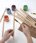 Holding a Premium Smooth Bamboo Wood Dowel Rod, 1/2 X 15 Inch, for crafting with paint jars and tools nearby.