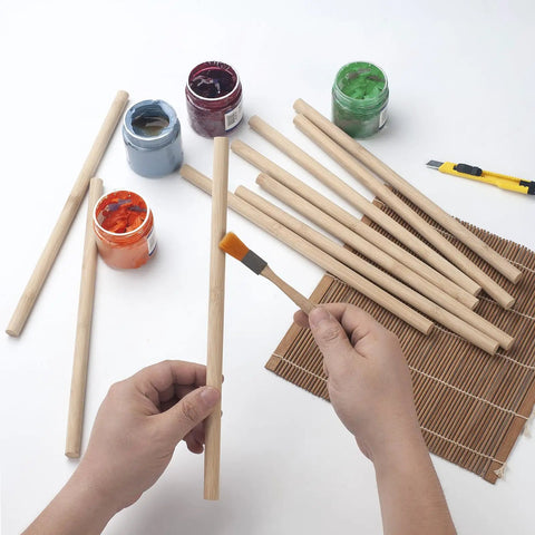 Holding a Premium Smooth Bamboo Wood Dowel Rod, 1/2 X 15 Inch, for crafting with paint jars and tools nearby.