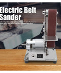 Torch Mini Electric Belt Sander Grinder Machine For Polishing And Smoothing Metal Or Wood Projects Compact Desktop Tool With Versatile Sanding And Wheel Modes For Home Workshop Use Stainless Steel Construction, side view on wooden surface.