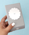 Hand holding 2.25 Inch Scalloped Circle Punch for Scrapbooks and Card Making, large white craft punch tool against a blue background.