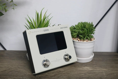 Ampero Mini MP50VN Guitar Multi Effects Processor With Touch Screen Modeling IR Cabinets shown on a table with potted plants.