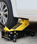 Side view of yellow floor jack with cushion pad lifting a white car; pinch-weld protector on frame.