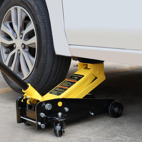 Side view of yellow floor jack with cushion pad lifting a white car; pinch-weld protector on frame.