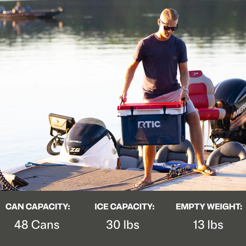 Man carrying Ultra Light 32 Quart Cooler That Weighs 30 Percent Less Than Rotomolded Coolers on a boat dock at sunset.