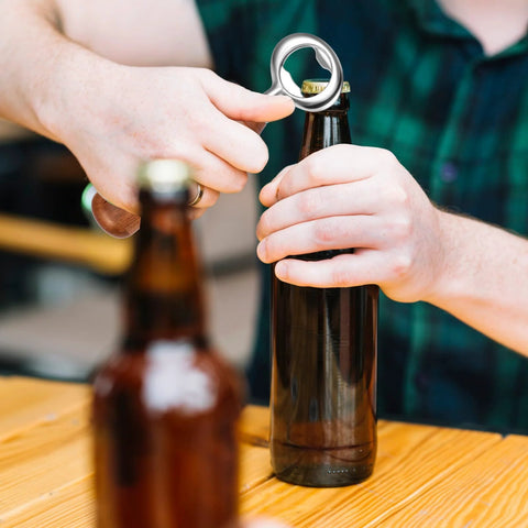 Front view of a silver stainless-steel bottle opener from an 8-piece kit used on a beer bottle.