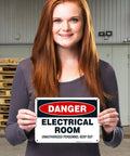 Hella Tough Aluminum Electrical Room Sign For Indoor And Outdoor Areas Killer Rust Proof Coating held by a woman in a warehouse.