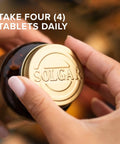 Close-up of hands opening a bottle with gold cap, labeled 'Solgar', showing a calcium complex for strong bones, 120 tablet pack.