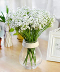 Artificial flower bouquet in a clear glass vase with rope accent, brightening a wooden table decor.