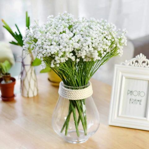 Artificial flower bouquet in a clear glass vase with rope accent, brightening a wooden table decor.