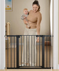 Woman with baby demonstrating Extra Wide Baby Gate For Stairs And Doorways Fits 27 To 43 Inches With Walk Through 21 Inch Opening 30 Inch Tall Auto Close Safety Gate For Dogs Includes Extenders And Hardware Mount Kit Black in doorway.