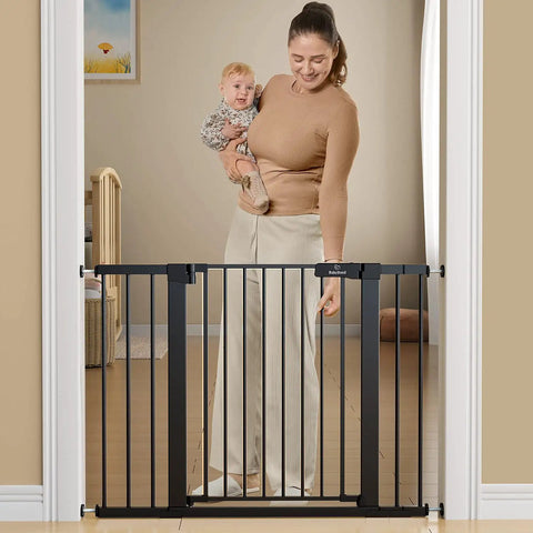 Woman with baby demonstrating Extra Wide Baby Gate For Stairs And Doorways Fits 27 To 43 Inches With Walk Through 21 Inch Opening 30 Inch Tall Auto Close Safety Gate For Dogs Includes Extenders And Hardware Mount Kit Black in doorway.