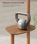 Close-up of the storage shelf on a freestanding coat rack with eight hooks in caramel brown, holding a small kettle bell weight.
