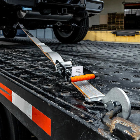 Close-up of Ultimate Axle Tie Down Kit with Silver Series Webbing on flatbed trailer for heavy duty hauling, abrasion resistant wear pad.