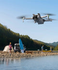 Mini 3 Fly More Combo Plus With RC Included Foldable Camera Drone flying over a riverside campsite with people and SUV