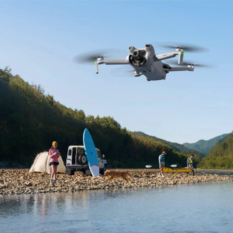 Mini 3 Fly More Combo Plus With RC Included Foldable Camera Drone flying over a riverside campsite with people and SUV