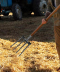 Person using Heavy Duty 11 Inch Four Prong Steel Pitch Fork Replacement Head for soil loosening on a farm