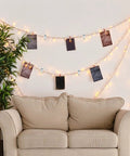 Cozy living room setup with string lights and photos hanging on wires above a beige loveseat and a green houseplant.